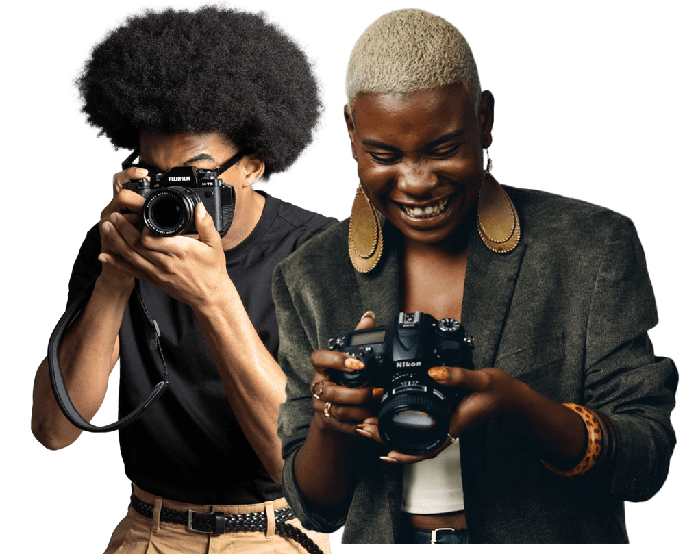 Zwei Personen nebeneinander. Die linke Person hält mit beiden Händen eine Kamera vor ihr Gesicht. Die rechte Person schaut lächelnd auf die Kamera in ihren Händen.